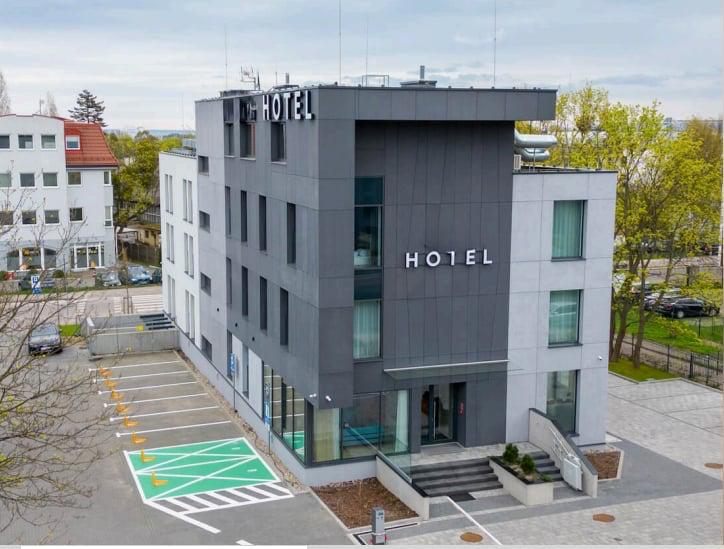 Nowoczesny budynek hotelu z napisem HOTEL, szklanymi oknami i parkingiem przed wejściem.
